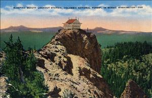 A saturated color postcard shows a small wooden structure with windows on all four sides perched on top of a rocky peak looking out over forests and rolling hills. 