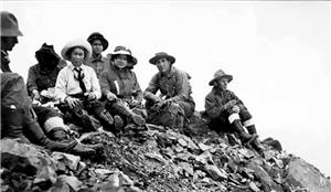 Seven men and women sitting on a rock in early 20th century hiking clothes and boots