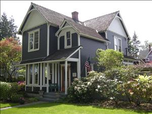 A two story victorian home with many architectural details. There are flowering bushes around the front of the house. 