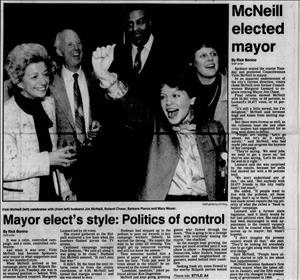 A newspaper headline shows five people three women one black man and one white man smiling and cheering. The headline says McNeill Elected Mayor