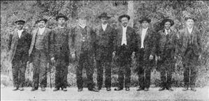 Nine men, most or all of them African American, in suits and hats stand in a row
