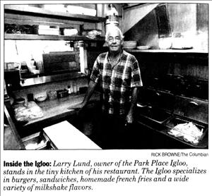 A man in a plaid shirt stands in a small restaurant kitchen