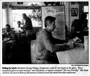 Newspaper clipping shows man sitting at diner counter reading the paper. Customers sit at booths behind him. 