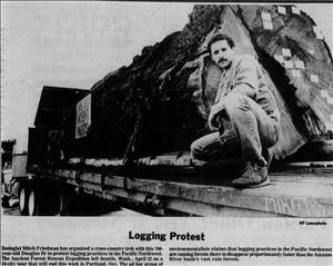 A man kneels on a truck bed next to a giant log