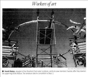 A newspaper clipping shows a circular metal sculpture surrounded by scaffolding on which construction workers are standing. 