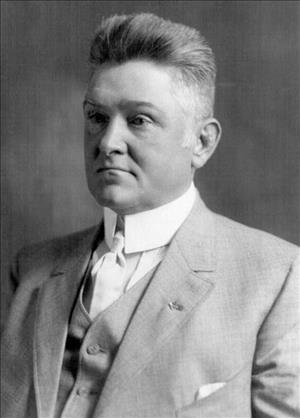 Black and white head-and-shoulders portrait of man in suit jacket, vest, and white tie and shirt