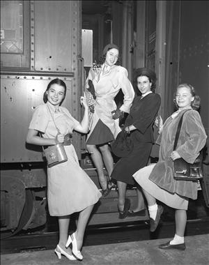 Four women pose in the door to a mid twentieth century passenger train. 