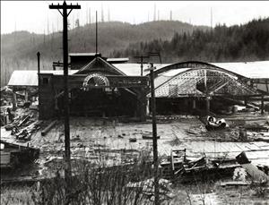 Wooden buildings starting to collapse at the base of forested and clearcut hillsides. One building has a sign that says Walville Lumber Company. 