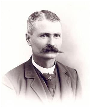 Taylor posing in a suit with a mustache and parted hair