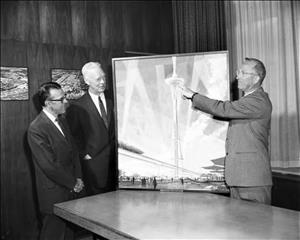 In a wood paneled meeting room, three men dressed in suits view a large artist's rendition of the Space Needle and Monorail
