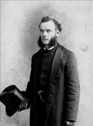 Blethen wearing mutton chops, a suit and holding a top hat in his hand
