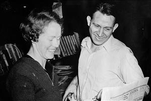Walter and Mildred Woodward smiling broadly, looking at a newspaper page with a linotype machine in the background