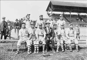 A team of ten players and a team captain all wearing the letter E on their chests on a very simple wooden bench in front of covered, wooden stands that are mostly empty