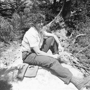 Buxbaum sitting outside on a rock wearing a button down shirt, trousers and checkered socks