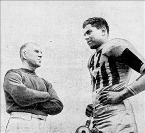 Harris standing in a football uniform with the number 47 on the chest next to another man with arms cross wearing a sweatshirt, both are looking in the distance in opposite directions