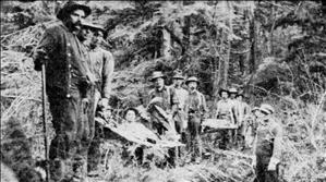 A party of thirteen in workwear holding two long stretchers in dense forest