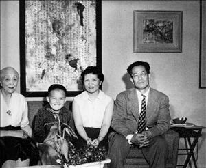 Dusanne sitting on a couch with a family of three in front of a large picture frame of torn paper containing Japanese text