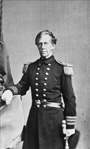An older Wilkes posing in military uniform with epaulettes, brass buttons and white gloves, leaning on a ledge covered in cloth