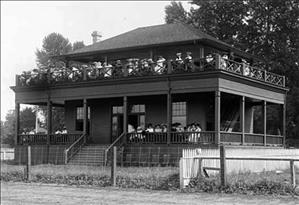 Photograph of two-story clubhouse at The Meadows racetrack in Georgetown. Racing fans can be seen on the ground-floor porch and on the balcony overhead