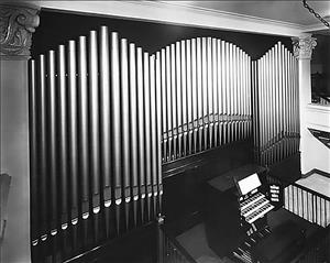 A wall of organ pipes tower over an organ. 