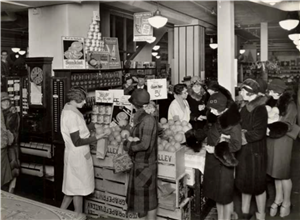 Several women in coats and hats stand around a fruit display in a store. 