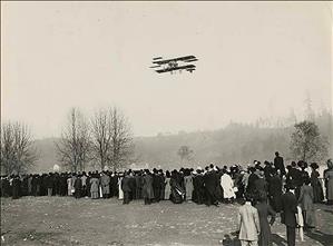 A biplane flies low over a large crowd looking up. 