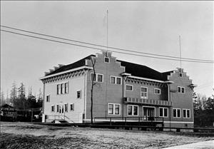 A large wooden building with architectural details along the roof line. There are trees in the background. 