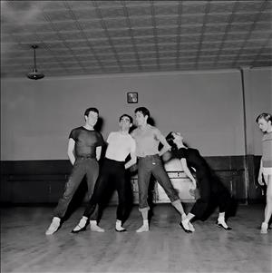 Four dancers lean towards each other in a dance studio. 