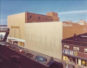 A concrete building with no windows and a large sign that says Rhodes. Cars are parked in front of the building. 