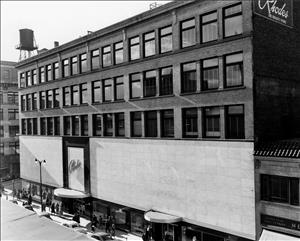 A six story building with many windows and a large sign over the door that says Rhodes. 