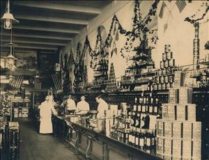 Four men stand on either side of a long wooden counter inside a grocery store with many products on display. 