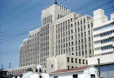 A tall art deco style building with many windows. Power lines criss cross in the foreground. 