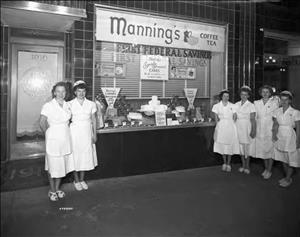 Wait staff standing outside in white uniforms in front of a store front with a sign reading "Manning's Coffee and Tea"