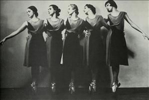 Five ballerinas on toe shoes stand with in a row with their arms around each others waists. 