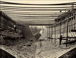 The inside of a ship under construction with long wooden frames meeting in the middle. 