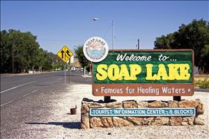 Color image of a sign that reads Welcome to Soap Lake Famous for Healing Waters. The sign is next to a paved road.