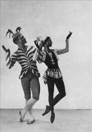 Two dancers in costumes and face make up hold their hands up and face to their left. 